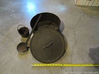 Full view of the antique cast iron pot with its lid, long-handled ladle, and smaller pot arranged next to a measuring tape showing size, on a concrete floor.