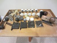 Top view of assorted antique door hardware including glass and porcelain knobs, mortise lock plates, and brass entry sets arranged on wooden table.