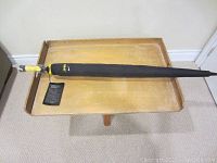 Photo of new black Nike golf umbrella with yellow and black handle lying on wooden tray.
