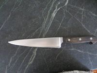 Full side view of the knife showing the entire blade and handle on black marble surface.