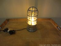 Retrofitted explosion proof industrial lamp on a wooden surface with the lamp turned on, showing illumination and cage structure.