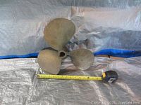 Used brass ship's propeller with three blades, approximately 12 inches in diameter, shown next to a measuring tape for size reference.