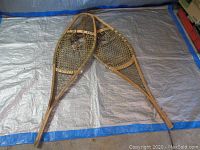 Pair of antique wooden snow shoes with hardwood frames and rawhide webbing placed on a tarpaulin background, showing both snow shoes overlapping at the center.