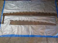 Two antique crosscut saws laid flat on a white tarpaulin. The larger 60-inch saw has wooden handles on both ends, shows significant rust and worn teeth. The smaller 54-inch sawblade lacks handles but also shows rust and aged metal.