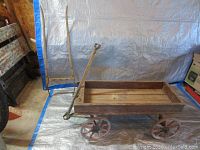 Side view of the antique children's wooden wagon with handle and yoke harness standing beside it.