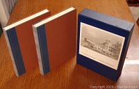 Two hardcover volumes and slipcase shown from above on wooden table, blue spines, brown covers, slipcase with front black and white illustration