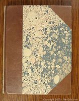 Front cover of book showing brown leather spine and corners with marbled paper covering main parts of the cover.