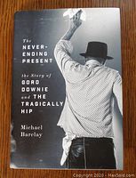 Front cover of the book showing Gord Downie from behind, raising a hand, wearing a checkered shirt and hat, with title and author printed.