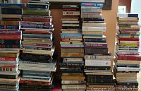 Photo showing large stacks of assorted books piled on a surface, covers and spines in various colors and genres visible.