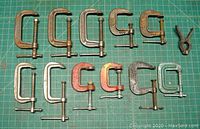 Photo showing 11 small clamps arranged on a grid surface with varying sizes and colors including metallic silver, orange, yellow, green, and a spring clamp.
