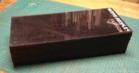 Stack of 36 rectangular dark tinted plexiglass sheets stacked neatly on a green cutting mat. Some sheets have white stick-on lettering on the edges. Sheets appear to be in good condition with a glossy finish.