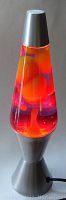Full view of an upright lava lamp with metal base and conical glass containing reddish-yellowish-orange wax blobs.