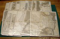 Photo showing the full set of 16 antique maps arranged overlapping on a wooden surface, covered with reflective protective plastic.