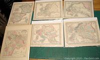 Overview of six antique hand-tinted maps laid out on green cutting mat