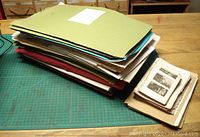 Large stack of assorted antique prints in various folders and loose, placed on green cutting mat