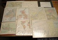Overview image of the 10 vintage maps arranged on a wooden table, all shrink wrapped or backed on cardboard or in magazine bags, showing various geographical regions.
