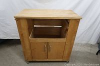 Front view of wooden kitchen cart showing butcher block style top, open middle shelf, and closed cabinet doors below.