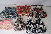 View of all six Vera Bradley handbags arranged on a white cloth background showing various colors and patterns