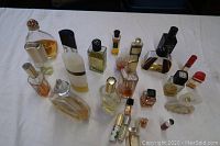 View of entire variety of perfume bottles on white cloth surface showing different sizes and shapes with clear to amber colored liquids.