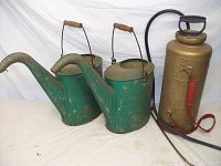Lot showing two green watering cans side by side and brass pump sprayer on right side; all items show signs of age and wear.