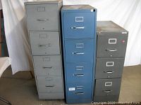 Three metal file cabinets standing side by side in different colors and sizes.