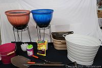 Full view of gardening pots, planters, stands, and gardening supplies on black table with white backdrop.