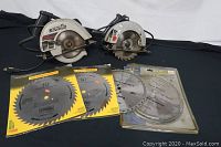 Two electric circular saws and several new saw blades displayed on black cloth