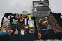 Wide view of table with large variety of tools, spray gun, clamps, gloves, and hardware materials spread out on a black surface.