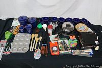 Full lot of assorted kitchen utensils, cookware, and gadgets including blue ceramic jars, muffin pan, spoons, thermometers, silicone cups, and cookware.
