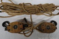 Two medium-sized wooden block and tackle pulley systems with attached coiled natural fiber rope, showing front view of the pulleys.