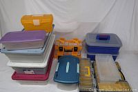 Photo showing an assortment of plastic storage containers and organizers in various colors including yellow, purple, white, blue, gray, and transparent plastic. Includes multiple stackable storage bins and smaller organizer boxes with compartments.