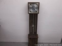 Full view of the tall wooden grandfather clock showing overall shape and pendulum