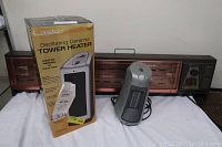 Three electric heaters side by side: boxed Asko tower heater, small silver ceramic heater, and large brown Lakewood heater.