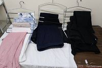 Photo showing several pairs of casual dress pants in a variety of colors and patterns, arranged on metal hanging racks and folded on a table.