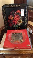 Photo showing the black painted metal floral tray and the boxed Christmas crystal platter on a table against a floral chair