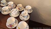 Nine china teacups with matching saucers arranged on a wooden surface, showing variety of floral patterns and gold trim.