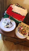 Photo of stacked Christmas kitchen linens in red and green and white, along with a plate and a Santa snow globe on a wooden surface.