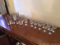 Photo showing all glasses lined up on wooden surface, including small wine glasses, highball glasses, and cocktail glasses with diverse gold foil and stamped designs.