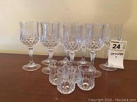 Eight crystal wine glasses arranged in a row, showing clear detailed cut pattern and faceted stems and bases. Four matching shot glasses arranged in front, smaller with the same cut pattern.