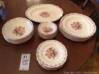 All items shown on a wooden table. Sets of stacked plates and bowls, plus a serving platter. Floral pattern and gold trim visible.