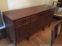 Sideboard from a side angle showing three drawers and three cabinet doors, wooden surface in brown finish.