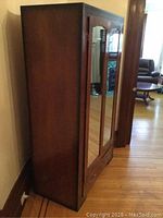 Side angle view of vintage wooden wardrobe armoire placed against wall. Shows dark wood finish and mirrored doors.