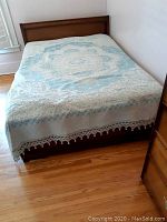 Full view of wooden bed frame with bedding including bedspread and pillow.