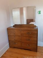 Front view of mid-century wood dresser showing six drawers with metal handles and attached large rectangular mirror reflecting room.