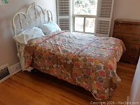 Full view of bed made with floral comforter and pillows, showing bed and part of dresser.