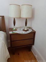 Nightstand with two lamps on top and doily beneath