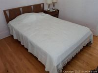 Bed fully made with white bedspread covering mattress and bedding, wooden headboard visible