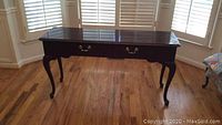 Single wooden sofa table in dark finish, rectangular with curved legs and one drawer with brass handles.