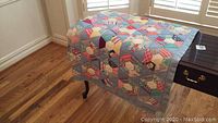 Quilt draped over a dark wooden table with visible hardwood flooring beneath. Shows full length and patchwork design.