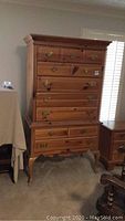Full view of the American Drew high boy dresser showing the front with drawers and brass hardware, placed near window blinds.